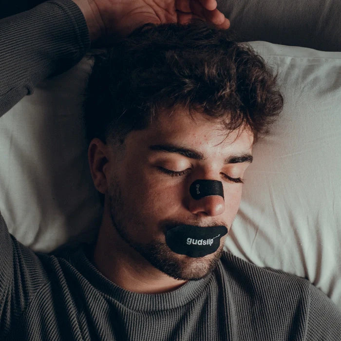 Muž spící s nosní páskou Gudslip, která přirozeně uvolňuje nosní cesty a zajišťuje volné dýchání bez chemie.